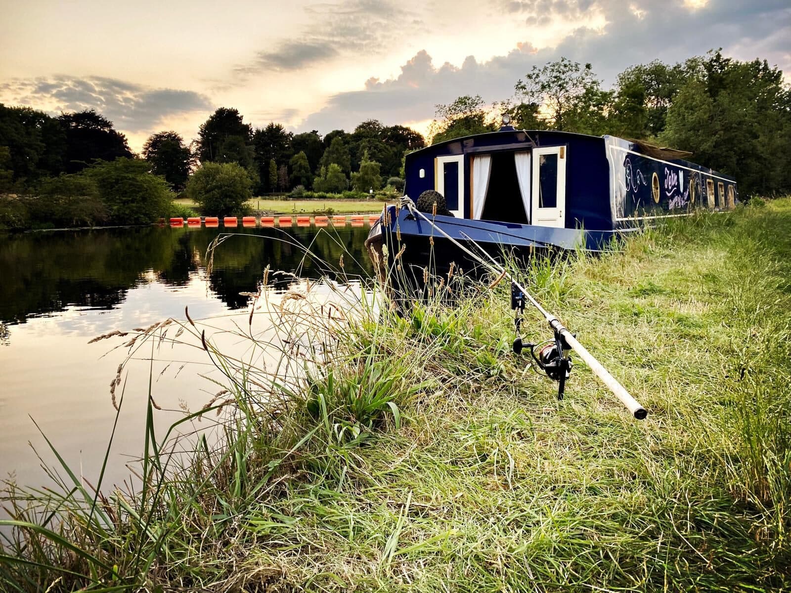 A narrowboat moored on a canal at sunset with a fishing rod on the bank