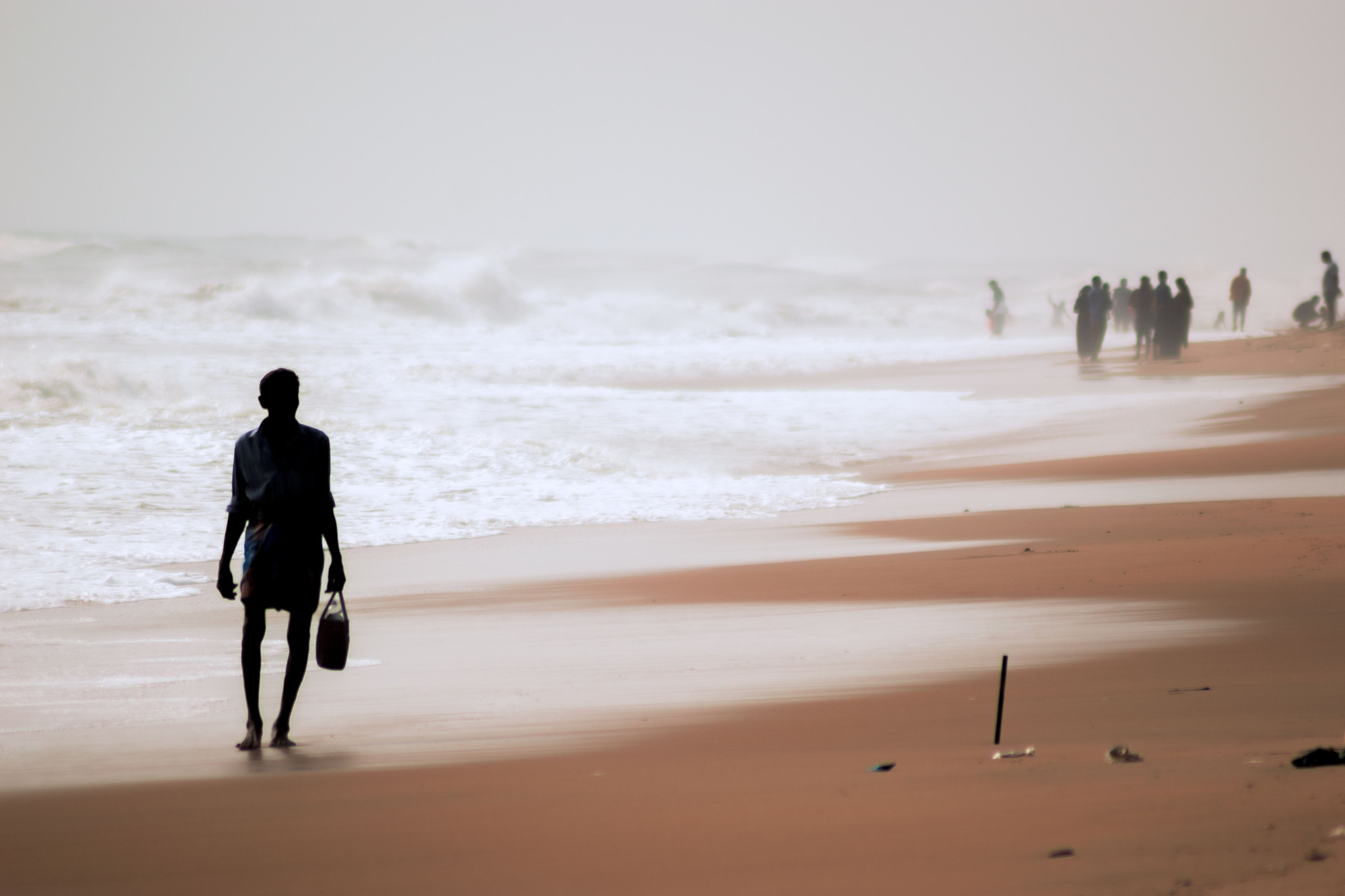 A man walking along the shoreline, with surf breaking behind him